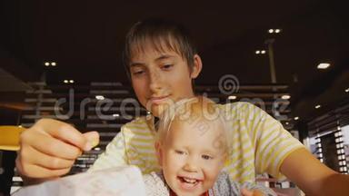 青少年吃快餐。 少年儿童和婴儿用快餐从袋子里取出炸薯条的特写镜头